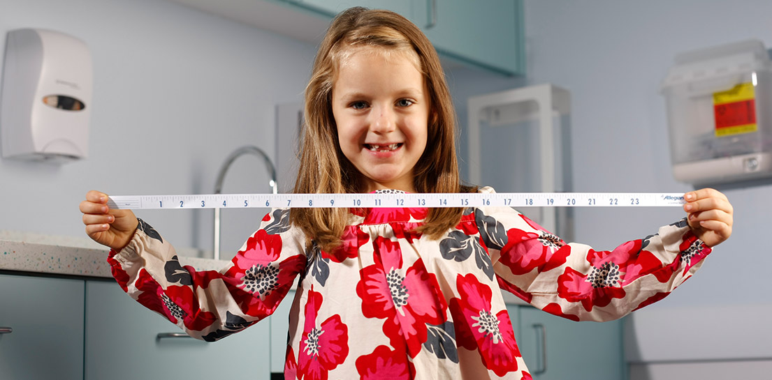 Smiling child holds a measuring tape with numbers in a medical room